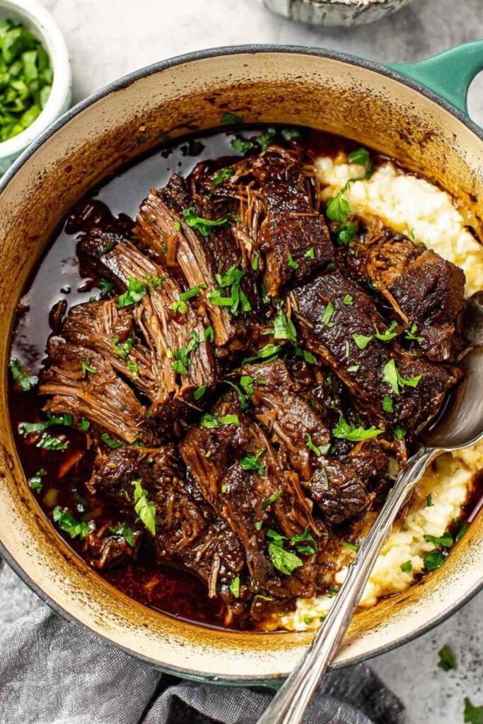Oven braised beef chuck roast shredded in braising liquid with carrots and herbs