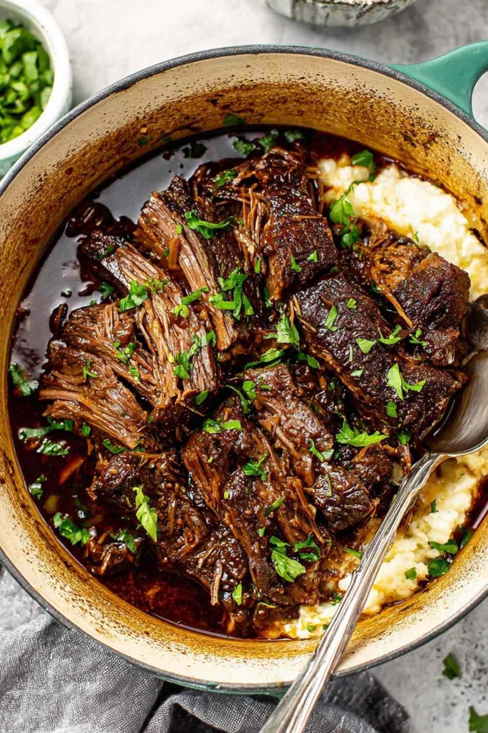 Oven braised beef chuck roast shredded in braising liquid with carrots and herbs
