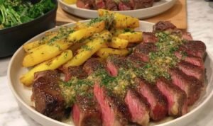 Sliced NY strip steak with truffle butter melting over the top, served with chimichurri fries and broccolini on a dinner plate