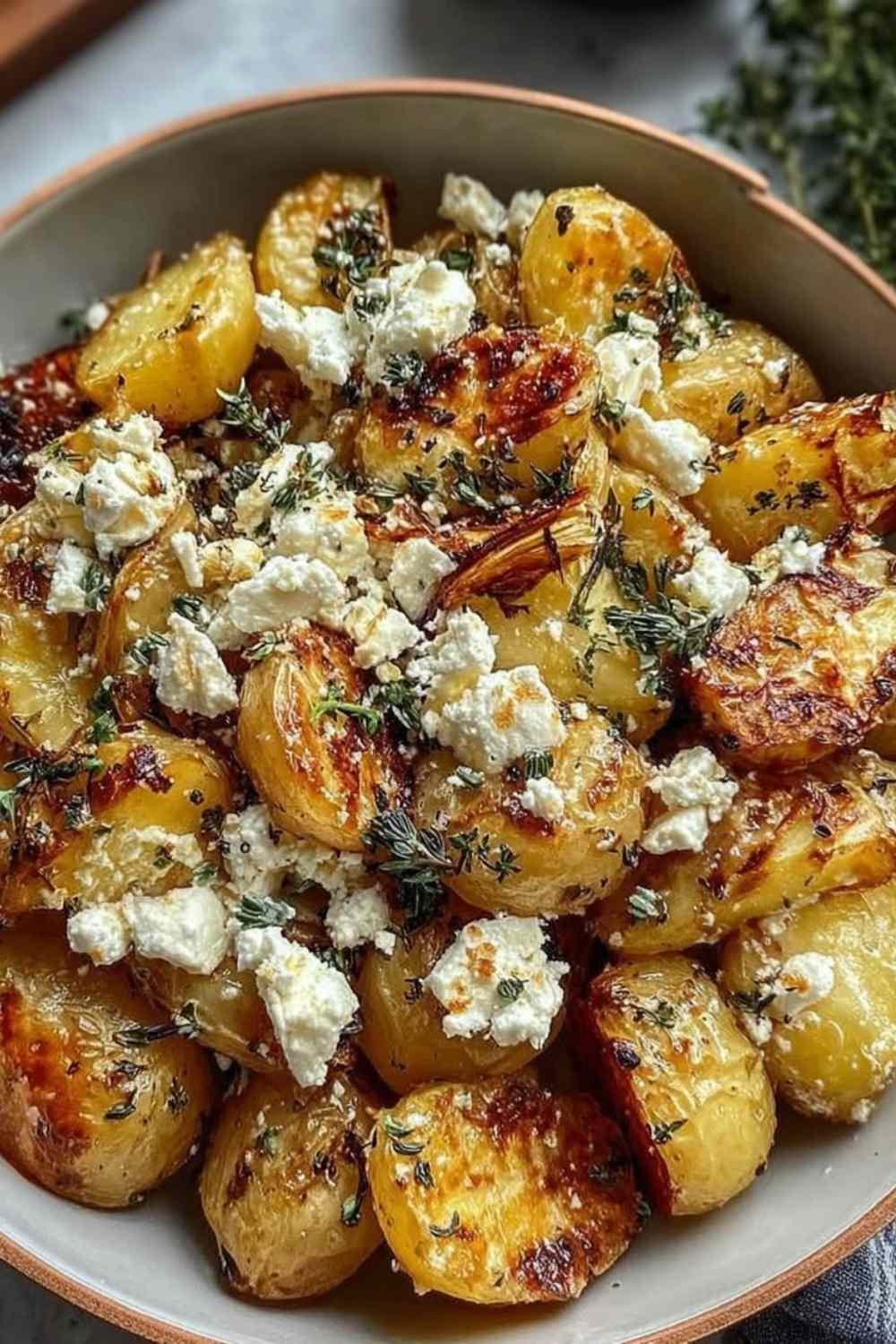 Roasted Potatoes with Baked Feta and Garlic in a white baking dish with fresh basil and honey drizzle