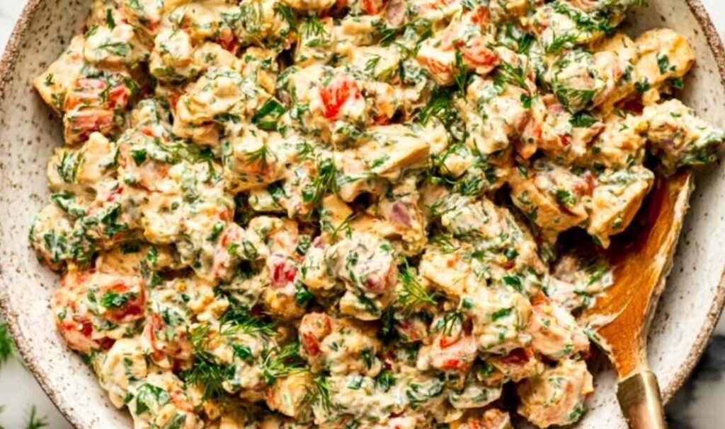 Bowl of spicy chicken salad with sriracha sauce, chopped scallions, red bell pepper, and fresh herbs on top