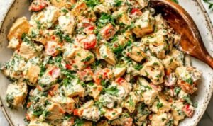 Bowl of spicy chicken salad with sriracha sauce, chopped scallions, red bell pepper, and fresh herbs on top