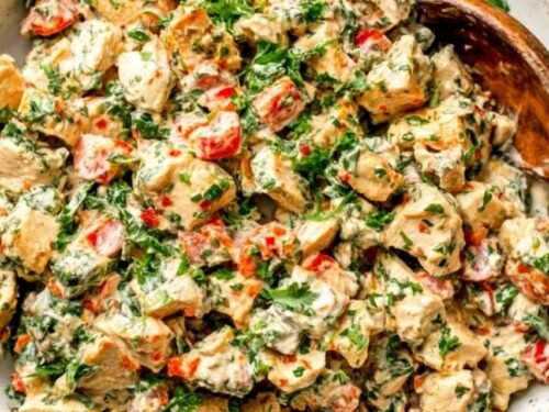 Bowl of spicy chicken salad with sriracha sauce, chopped scallions, red bell pepper, and fresh herbs on top