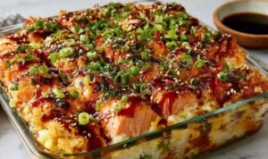 Spicy Salmon Sushi Bake Spicy Salmon Sushi Bake in a 9x9 baking dish topped with avocado, cucumber, green onions, and drizzle of mayo and unagi sauce