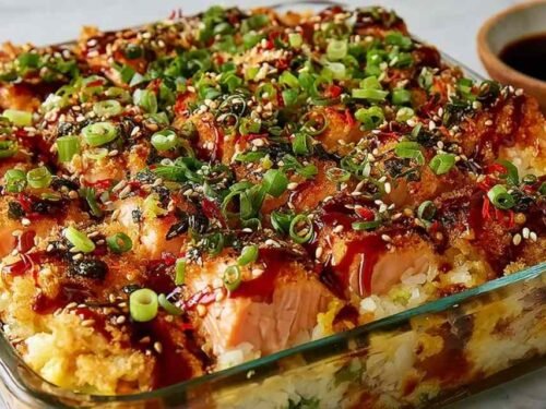 Spicy Salmon Sushi Bake in a 9x9 baking dish topped with avocado, cucumber, green onions, and drizzle of mayo and unagi sauce