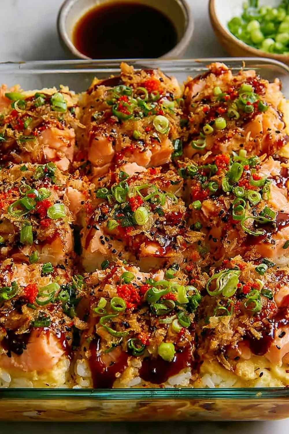 Spicy Salmon Sushi Bake in a 9x9 baking dish topped with avocado, cucumber, green onions, and drizzle of mayo and unagi sauce