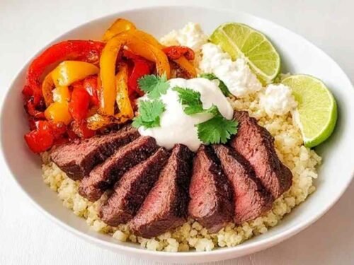 Steak Fajita Bowl with seared steak strips, caramelized peppers, avocado slices, sour cream, and fresh cilantro on a white bowl