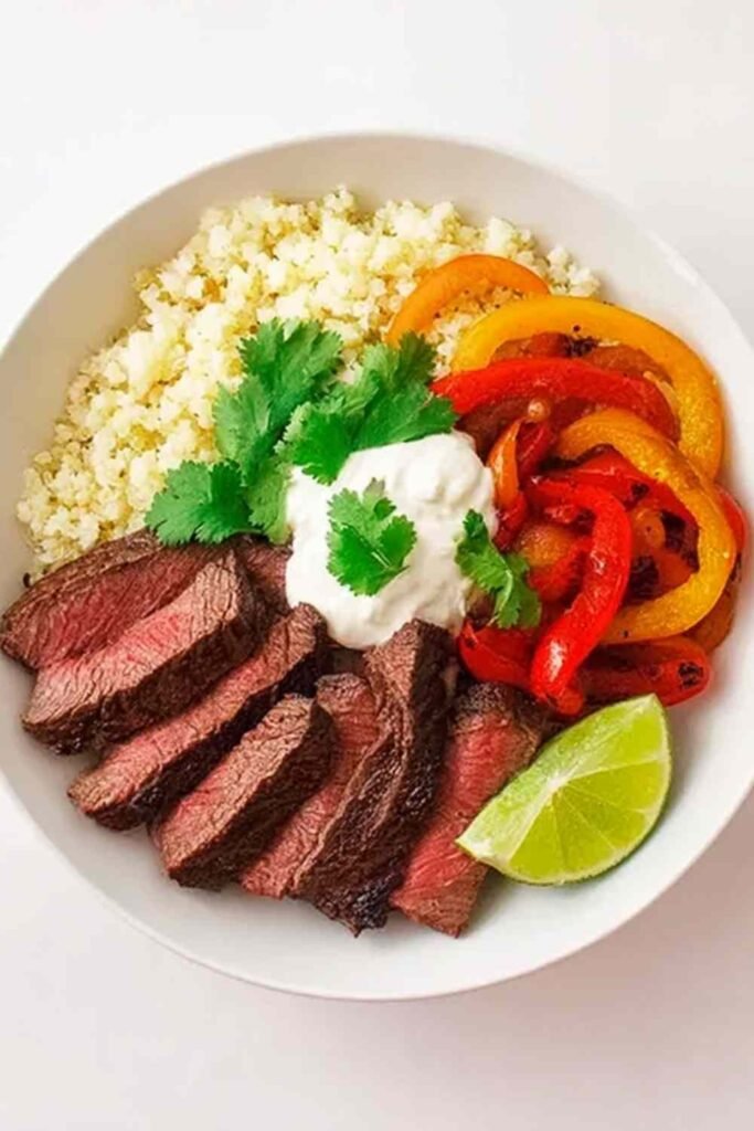 Steak Fajita Bowl with seared steak strips, caramelized peppers, avocado slices, sour cream, and fresh cilantro on a white bowl