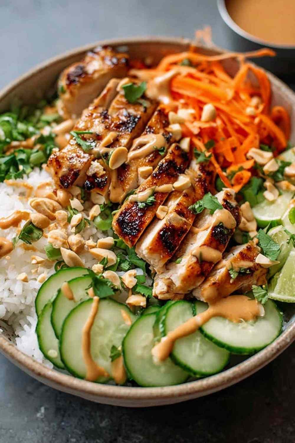 Thai peanut chicken buddha bowl with golden seared chicken breast strips, julienned carrots, cucumber, edamame, and creamy peanut sauce over brown rice