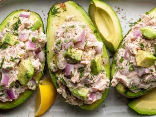 Avocado tuna salad boats filled with creamy tuna salad and garnished with fresh parsley on a white plate