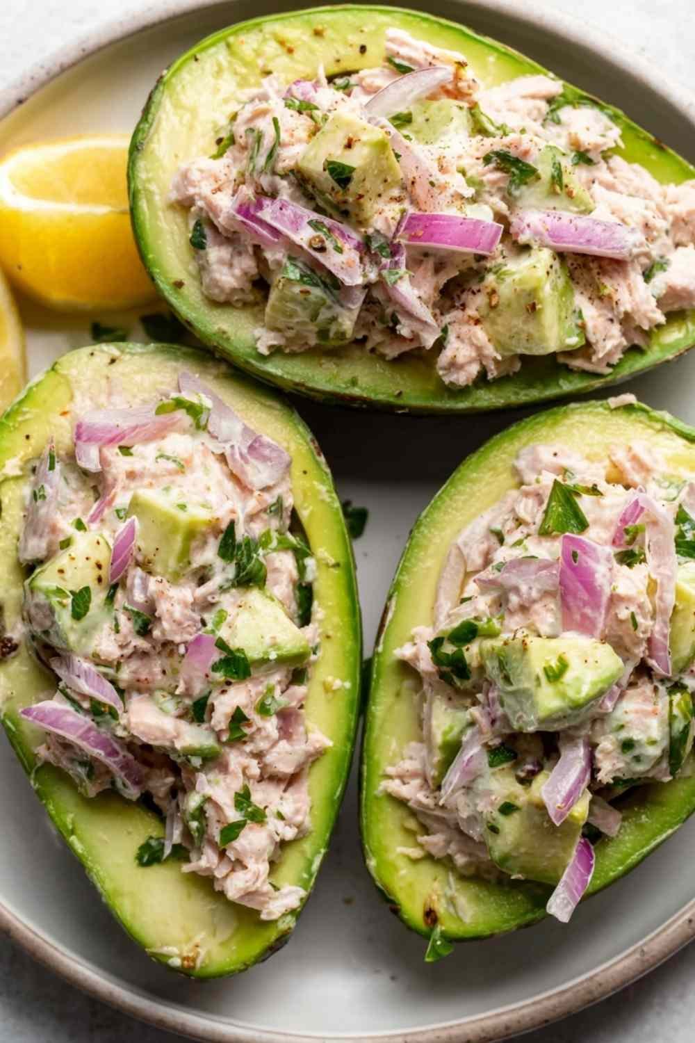 Avocado tuna salad boats filled with creamy tuna salad and garnished with fresh parsley on a white plate