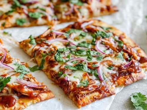 Freshly baked BBQ chicken crust pizza on a parchment-lined baking sheet, topped with melted mozzarella, crispy bacon, and red onion