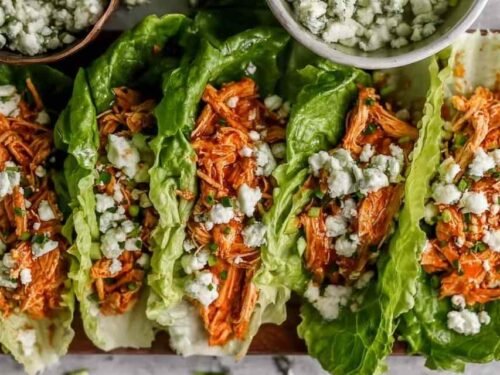 Close-up of buffalo chicken lettuce wraps topped with blue cheese and celery on a white plate