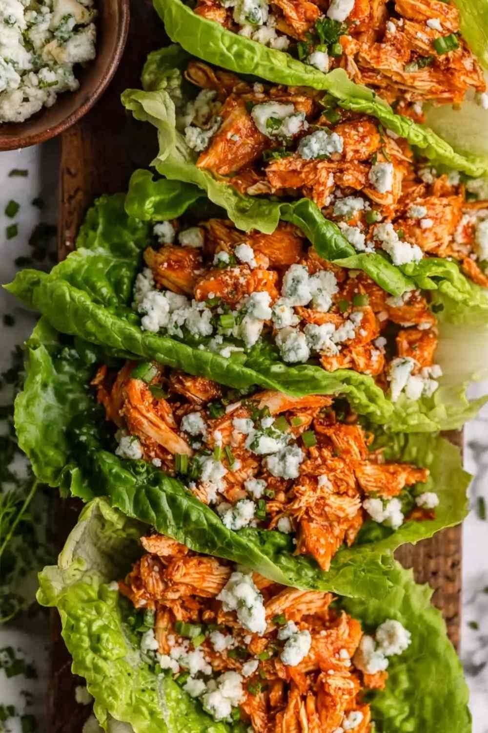 Close-up of buffalo chicken lettuce wraps topped with blue cheese and celery on a white plate