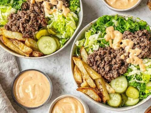 Overhead view of burger bowls with crispy potato chips, seasoned ground beef, shredded lettuce, cheese, pickles, and special sauce drizzle