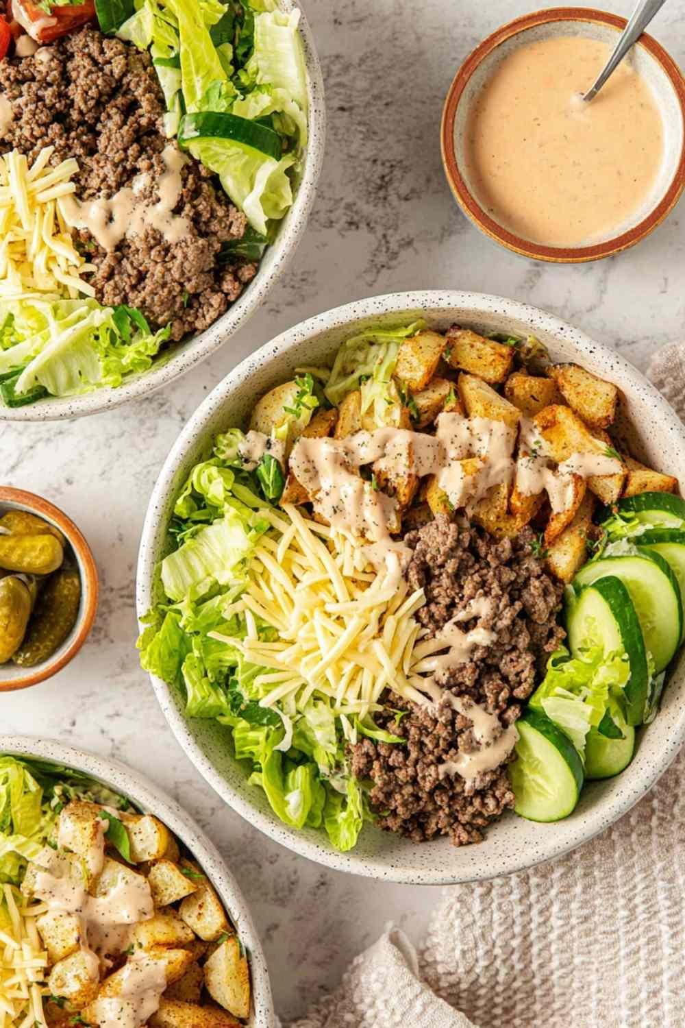 Overhead view of burger bowls with crispy potato chips, seasoned ground beef, shredded lettuce, cheese, pickles, and special sauce drizzle