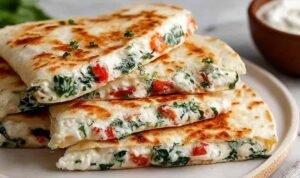 Mediterranean quesadilla cut into golden crispy wedges with feta, spinach, and mozzarella filling on a wooden cutting board