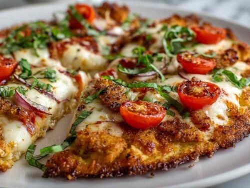Golden chicken crust pizza topped with melted mozzarella, fresh tomato slices, and basil on a parchment-lined baking pan
