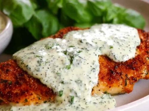 Breaded chicken cutlets being pan-seared in butter for Chicken in Basil Cream Sauce, golden and crispy in a large stainless steel skillet