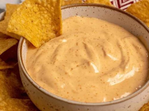 Creamy cottage cheese queso dip in a white bowl topped with pico de gallo, served with tortilla chips on a wooden board