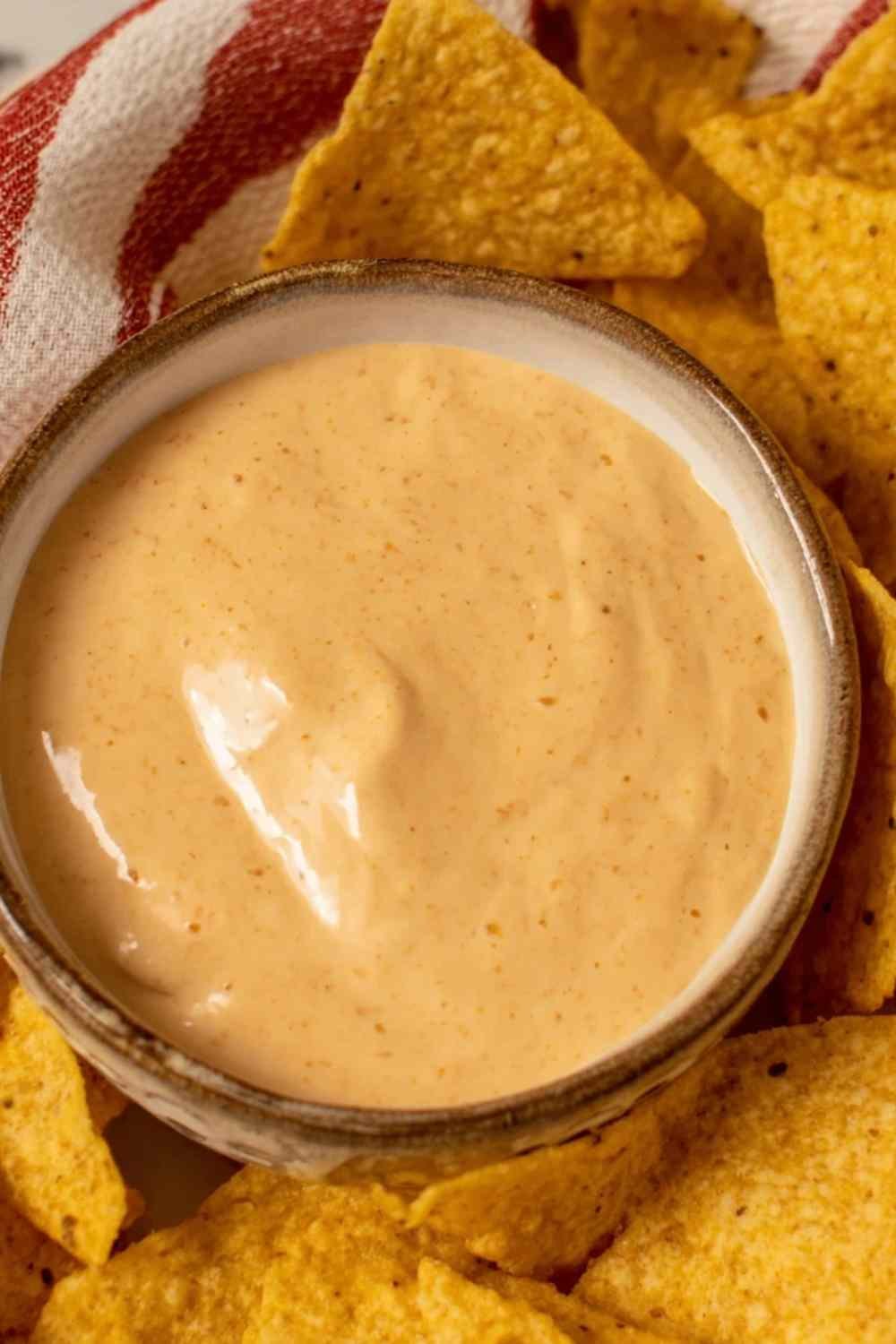Creamy cottage cheese queso dip in a white bowl topped with pico de gallo, served with tortilla chips on a wooden board