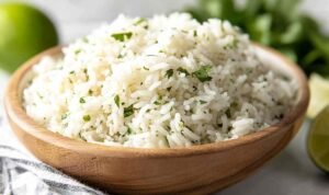 Bowl of copycat chipotle rice with fresh cilantro and lime on a wooden table