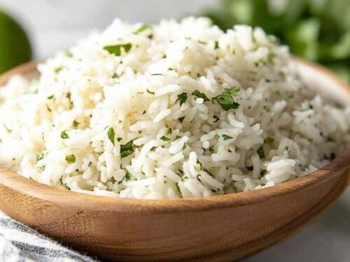 Bowl of copycat chipotle rice with fresh cilantro and lime on a wooden table