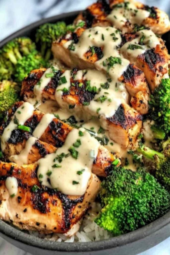 Grilled chicken and broccoli bowl with creamy garlic sauce served over brown rice in a white bowl