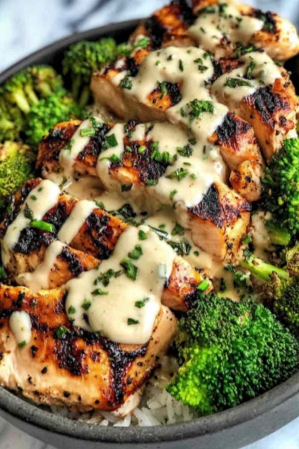 Grilled chicken and broccoli bowl with creamy garlic sauce served over brown rice in a white bowl