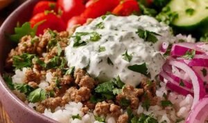Assembled ground turkey bowl with jasmine rice, cucumber, grape tomatoes, red onion, and creamy lemon dill yogurt sauce
