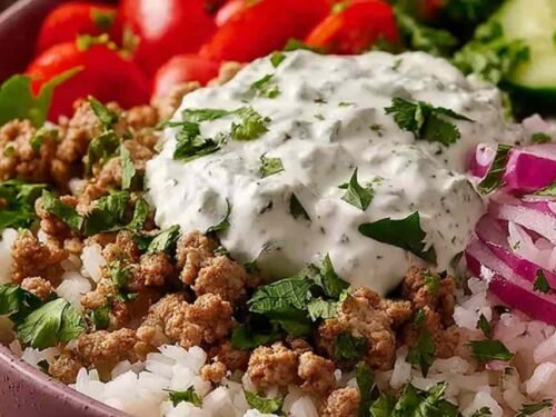 Assembled ground turkey bowl with jasmine rice, cucumber, grape tomatoes, red onion, and creamy lemon dill yogurt sauce