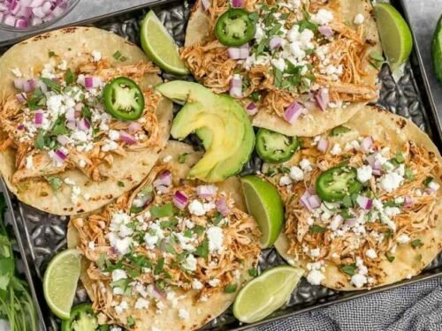 Healthy crockpot chicken tacos in flour tortillas with avocado, jalapenos, and lime on a wooden board