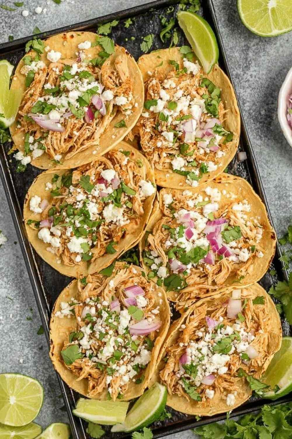 Healthy crockpot chicken tacos in flour tortillas with avocado, jalapenos, and lime on a wooden board