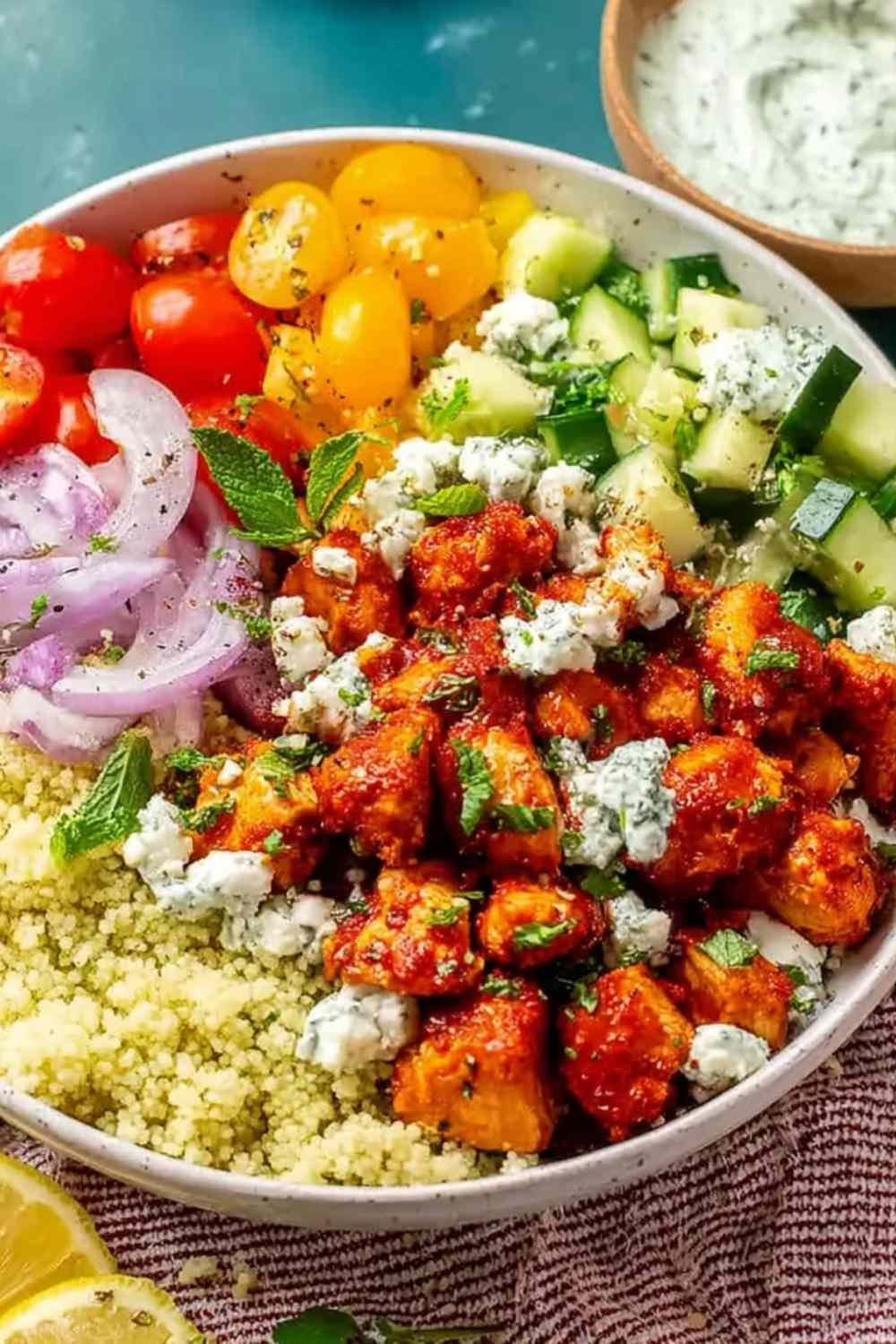 Four Mediterranean chicken bowls with harissa chicken, quinoa, tzatziki, and Greek salad on a wood table
