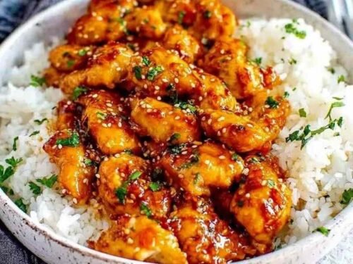 Close-up of honey garlic chicken thighs in a skillet with glossy sauce, garnished with parsley and chili flakes