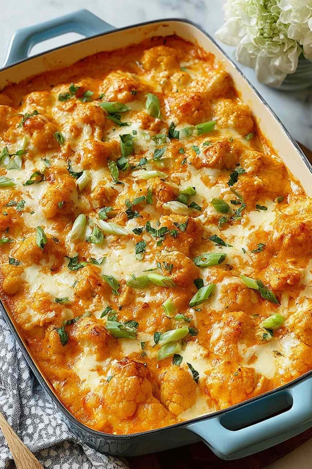 Freshly baked Buffalo Chicken Cauliflower Casserole with melted cheddar cheese and green onions in a white baking dish