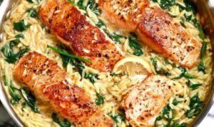 One skillet salmon with lemon orzo served in a large nonstick pan with wilted spinach, Parmesan, and chili flakes