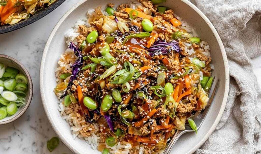 Turkey egg roll in a bowl cooking in a large skillet with coleslaw, carrots, edamame, and soy-sesame sauce