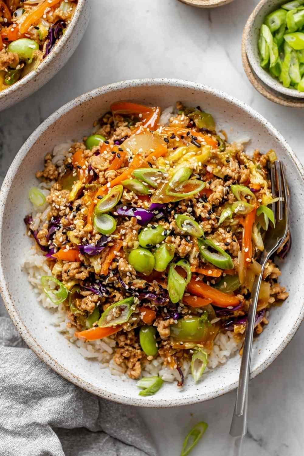 Turkey egg roll in a bowl cooking in a large skillet with coleslaw, carrots, edamame, and soy-sesame sauce