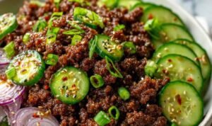 Spicy Keto Korean Ground Beef Spicy keto Korean ground beef in a bowl with gochujang sauce served alongside a fresh cucumber salad with sesame seeds
