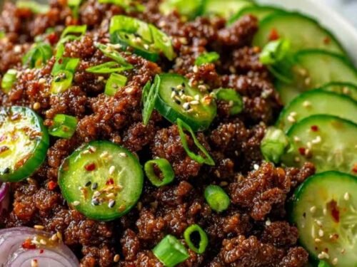 Spicy keto Korean ground beef in a bowl with gochujang sauce served alongside a fresh cucumber salad with sesame seeds