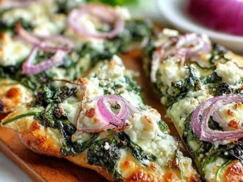 Spinach and feta flatbread pizza with melted mozzarella, crumbled feta, fresh spinach, and sliced red onion on a crispy flatbread crust