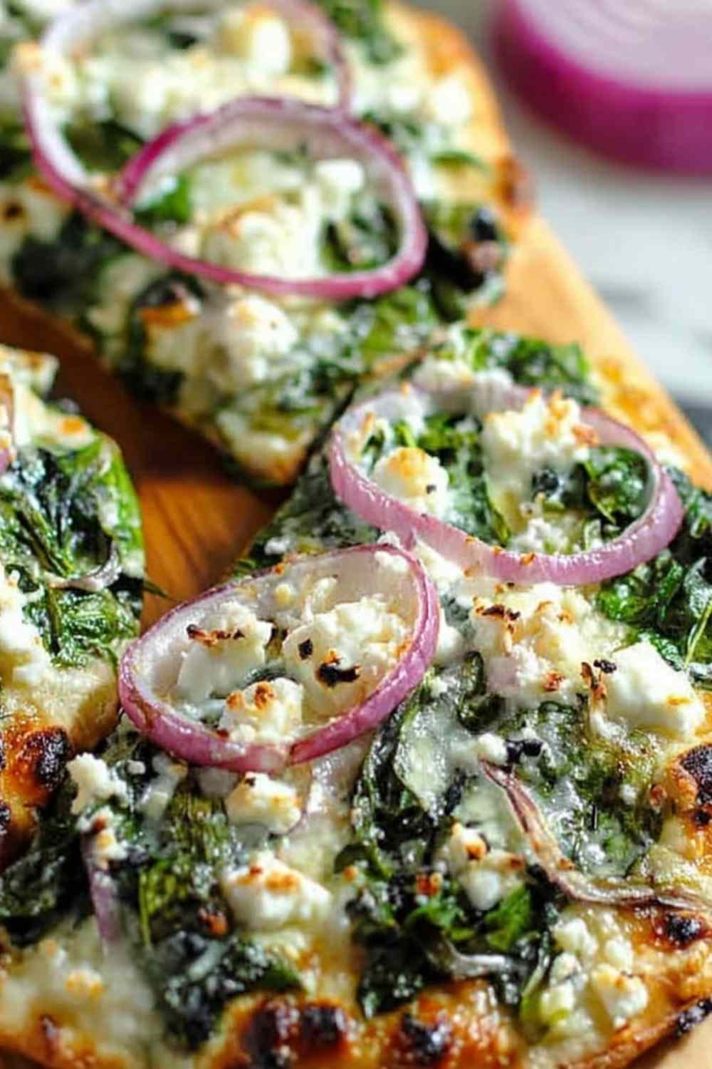 Spinach and feta flatbread pizza with melted mozzarella, crumbled feta, fresh spinach, and sliced red onion on a crispy flatbread crust